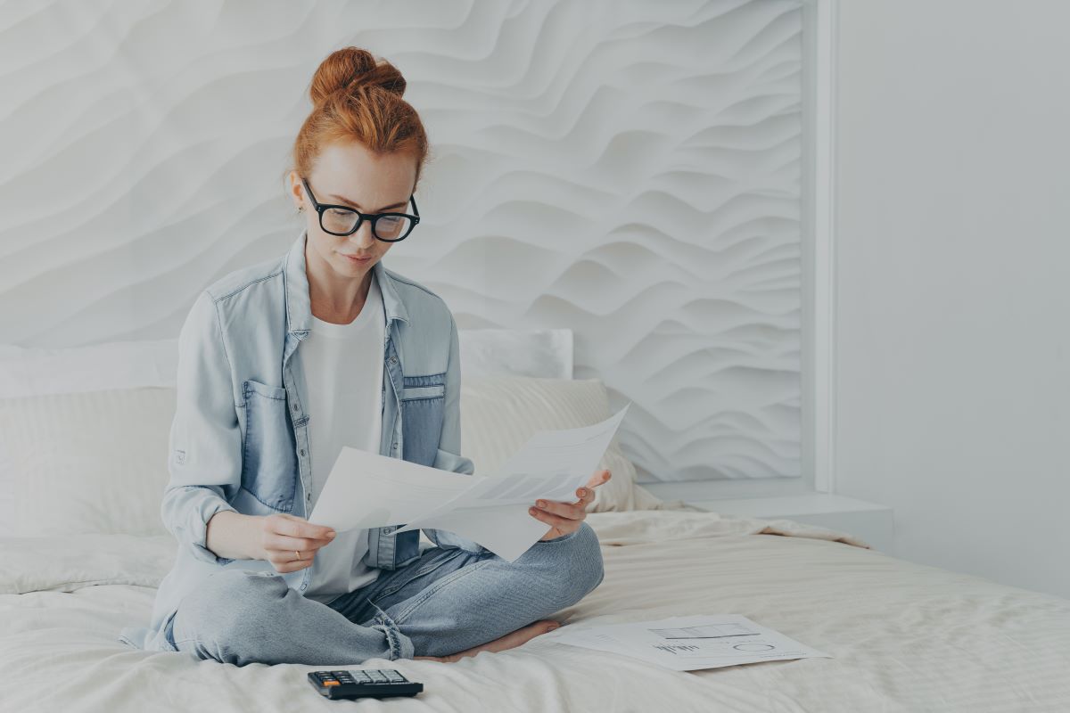 Une freelance assise sur son lit regarde des factures
