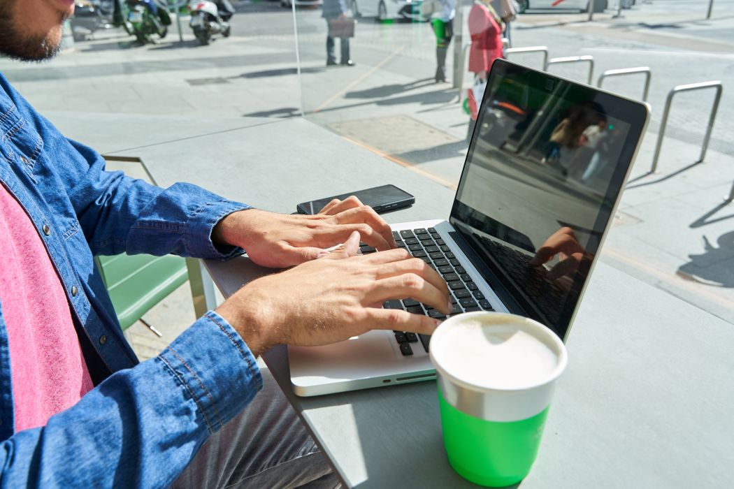 mains d'un homme assis dans un café utilisant son ordinateur portable pour travailler