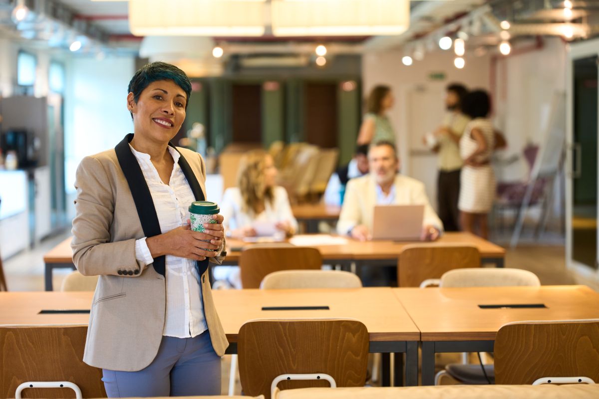 Femme d'affaires latine souriante tenant une tasse de café dans un bureau de coworking moderne<br>