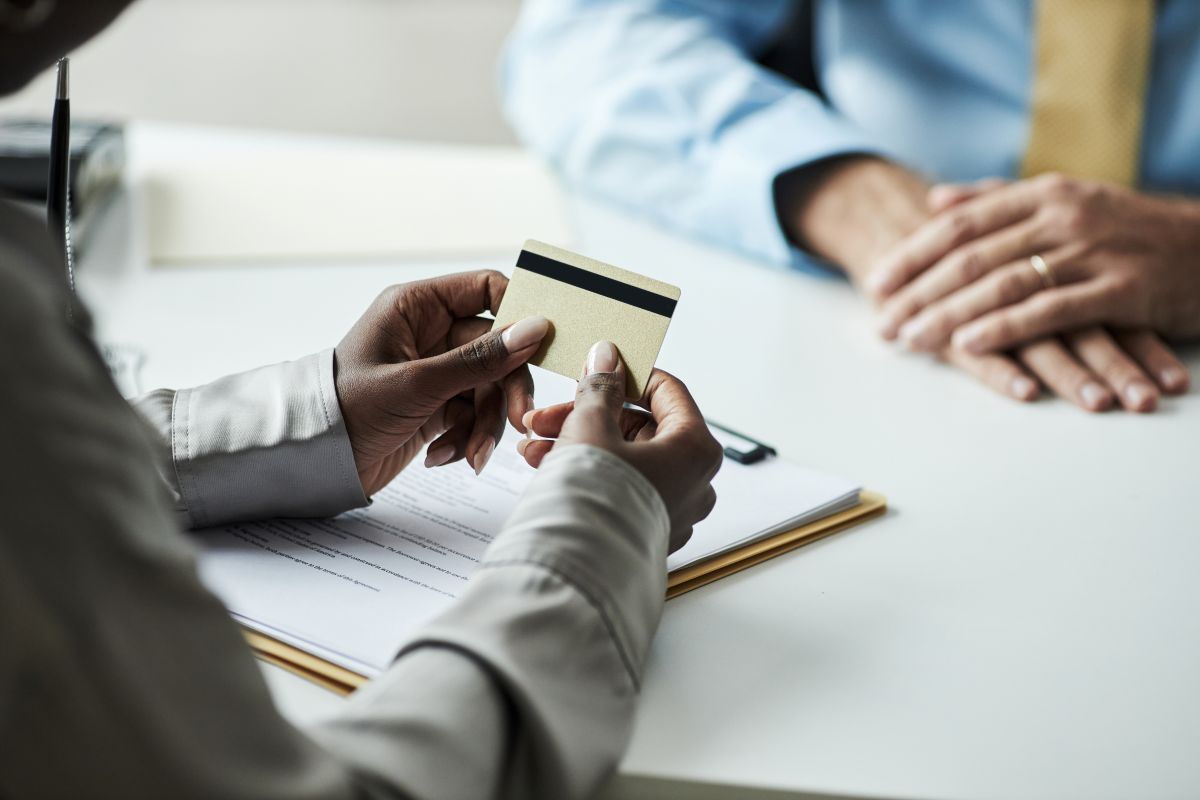 Une jeune femme tient une carte de crédit tout en consultant un employé de banque 