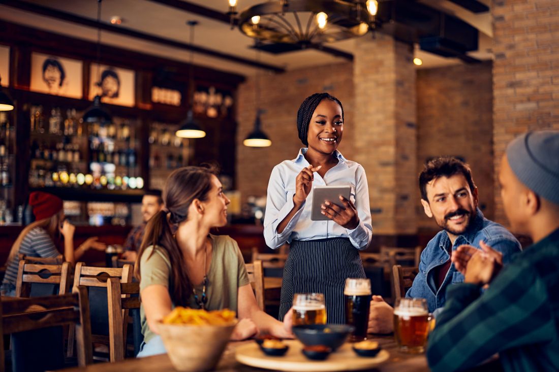 Une serveuse utilise un pavé tactile tout en prenant la commande de ses clients dans un bar. 
