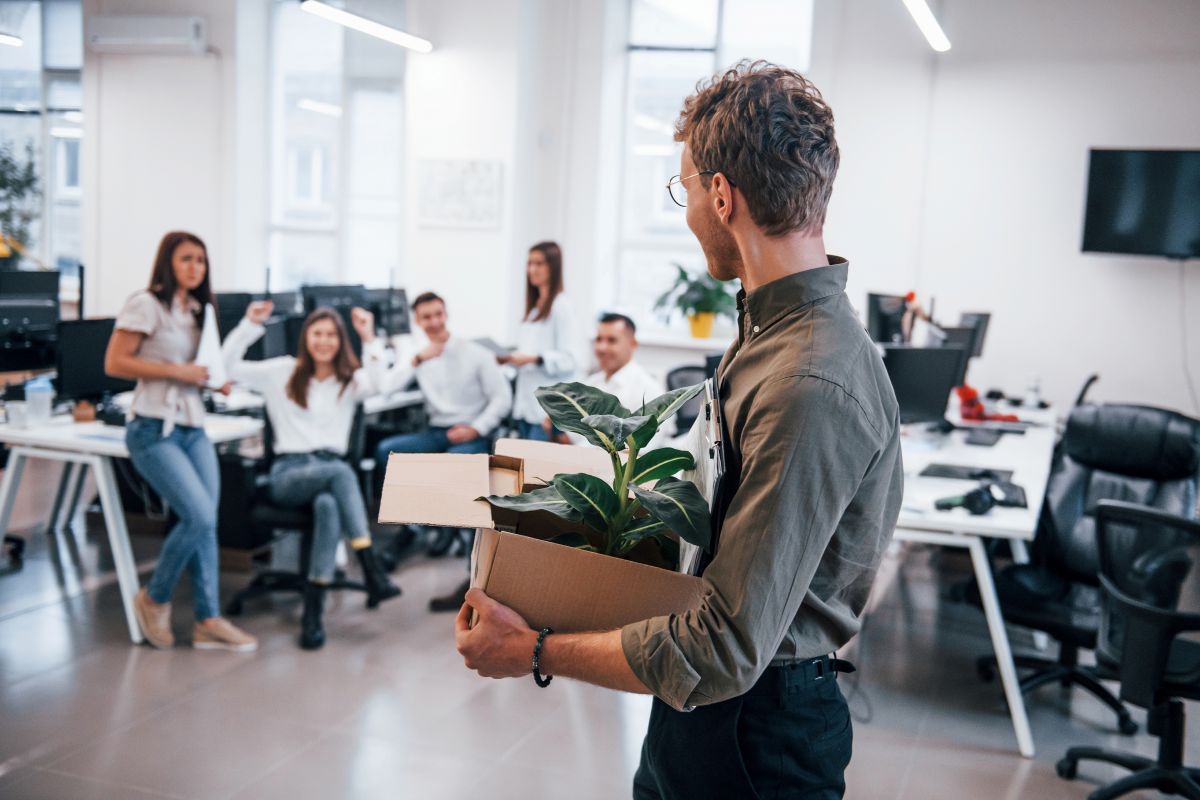 Homme élégant à lunettes tenant une boîte avec une plante devant ses collègues au bureau
